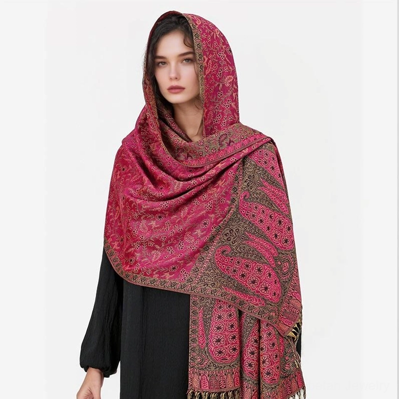 Model wearing rose pink Tibetan hooded paisley shawl with brown pattern details, side-front angle showing decorative patterned hem fringe and wrap styling