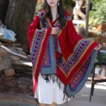 Tibetan red hooded poncho shawl with heart patterns and tassel fringe, front three-quarter view outdoors