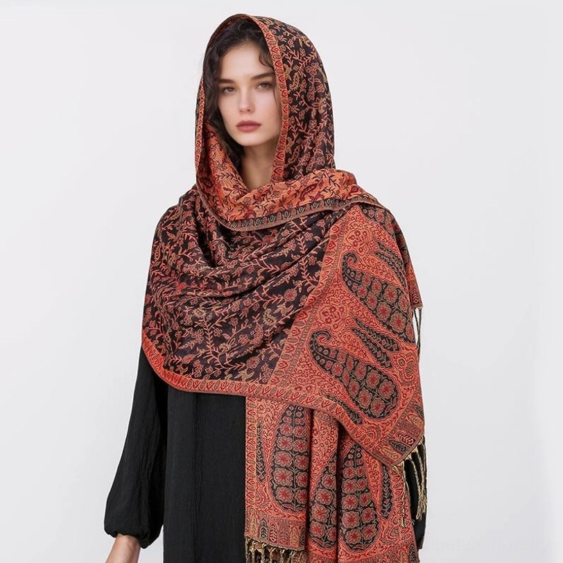 Model wearing terracotta orange and dark brown Tibetan hooded paisley shawl with bold side panel patterns, front view showing fringe hem detail