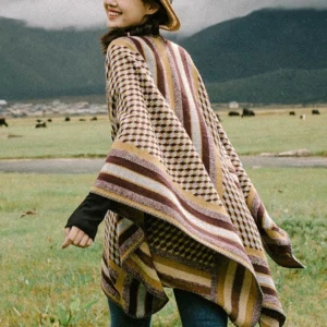 Tibetan houndstooth poncho shawl worn as rear three-quarter drape on model in mountain grassland, showing oversized fit and warm earthy tones