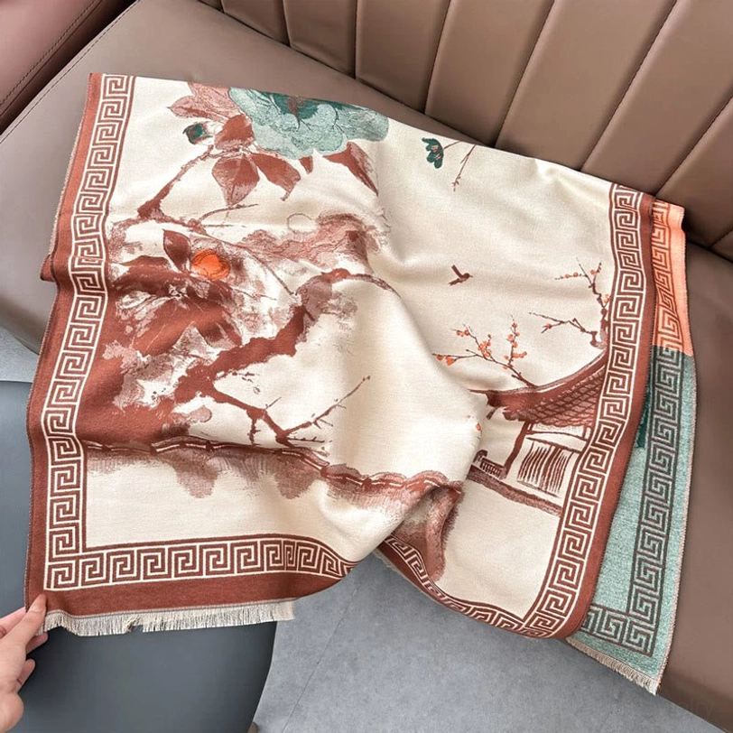 Handwoven Tibetan ink scarf laid flat on sofa, featuring cream base with brown geometric border and traditional pavilion floral design