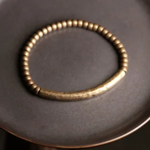 Artisan-made prosperity brass beaded bracelet displayed on dark ceramic surface, showcasing hammered central band and spacer beads