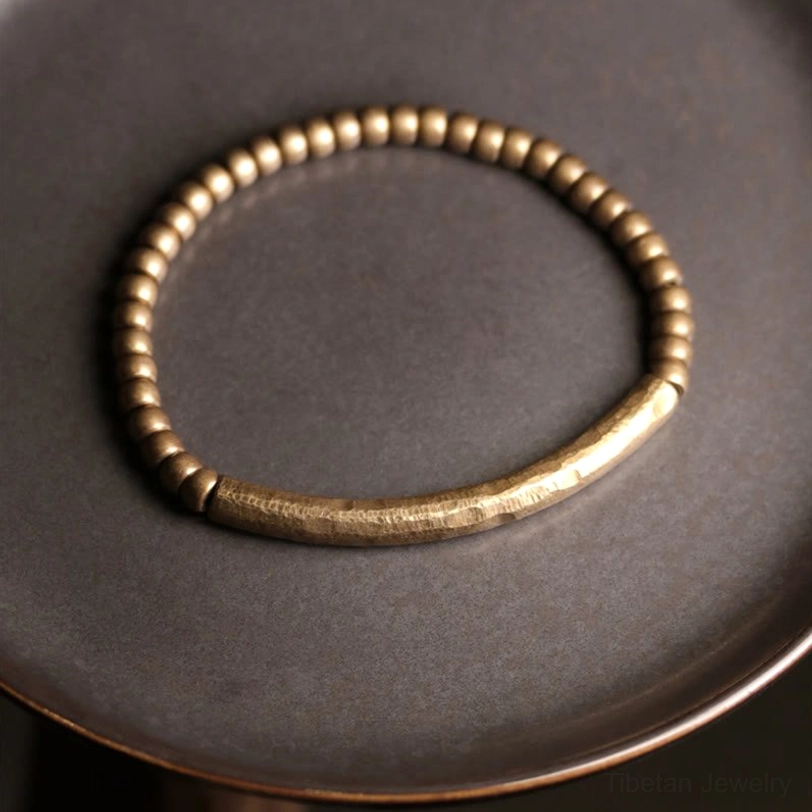 Artisan-made prosperity brass beaded bracelet displayed on dark ceramic surface, showcasing hammered central band and spacer beads