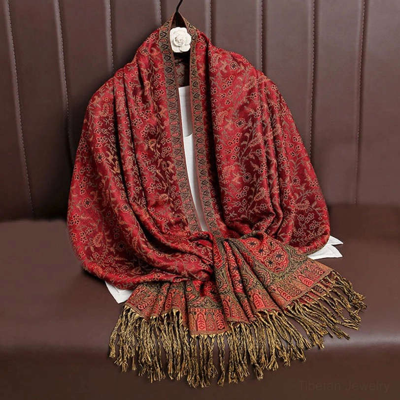Deep crimson Tibetan jacquard wrap with brown paisley accents and all-over woven texture, draped on sofa backrest showcasing fringe trim detail
