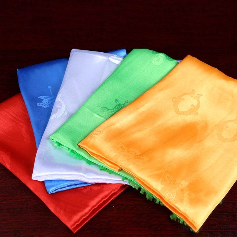Individual Tibetan khata scarves loosely arranged showing satin fabric and embossed blessing designs on wooden background