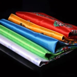 Stacked collection of five Tibetan khata scarves showing all traditional colors with intricate Buddhist auspicious patterns and glossy satin texture