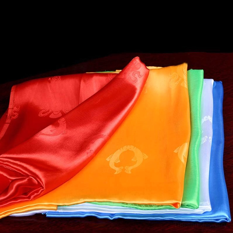 Fanned-out Tibetan five-color khata scarves on dark wood showing vibrant colors and draped satin texture with circular embossed motifs