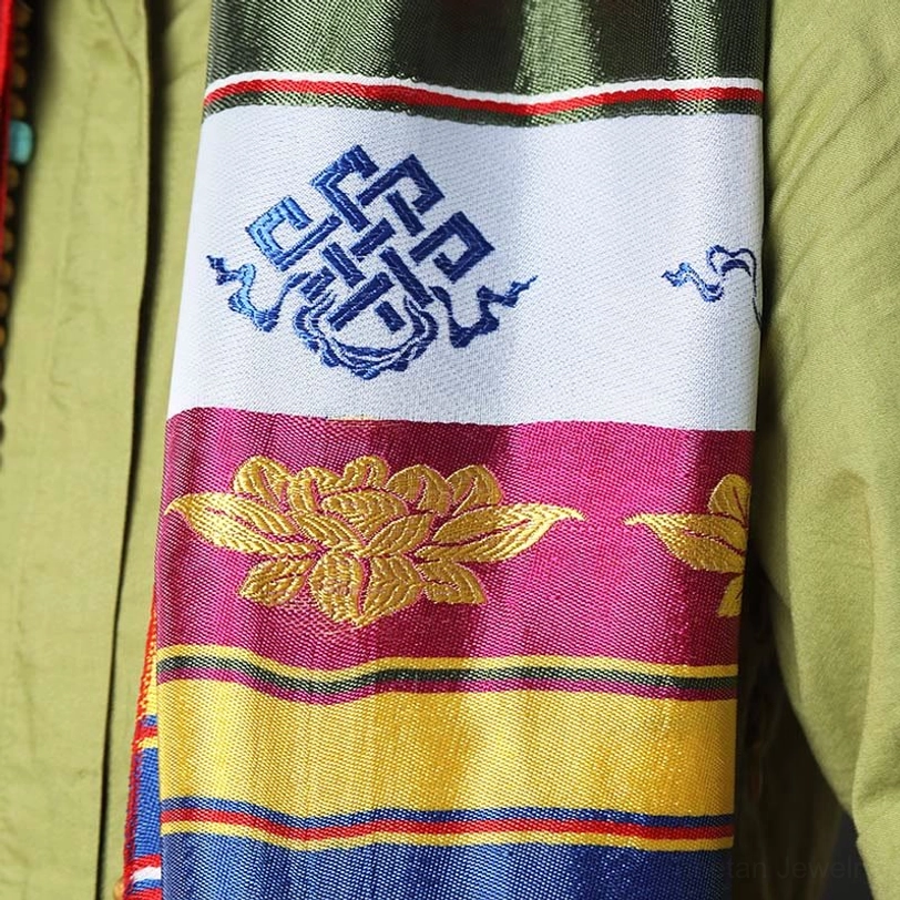Tibetan khata fabric close-up featuring golden lotus motif, endless knot embroidery, and vibrant color-block stripes