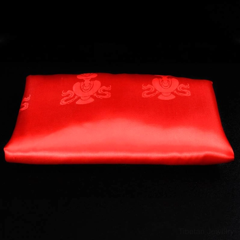 Single red Tibetan khata scarf with bright satin finish and red embossed blessing motifs on dark background