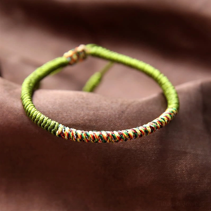 Green base Tibetan King Kong knot bracelet with multicolor woven accents and adjustable tassels, flat lay on satin background