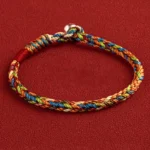 Tibetan King Kong knot multicolored woven bracelet with silver clasp, flat lay top-down view on red fabric background