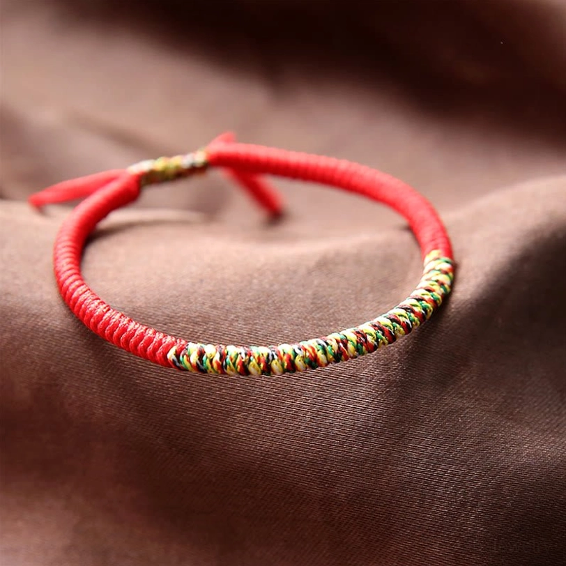 Red and multicolor Tibetan braided King Kong knot bracelet with adjustable closure, close-up flat lay view on satin fabric