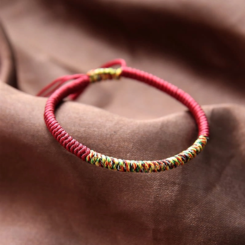 Handmade Tibetan King Kong knot multicolor braided bracelet with red base and adjustable tassel, flat lay on satin fabric