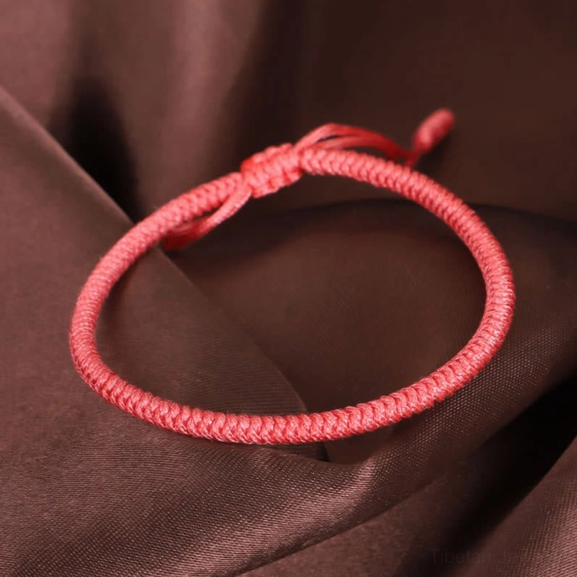 Single Tibetan King Kong knot braided bracelet in solid pink-red with tight woven texture on dark fabric background