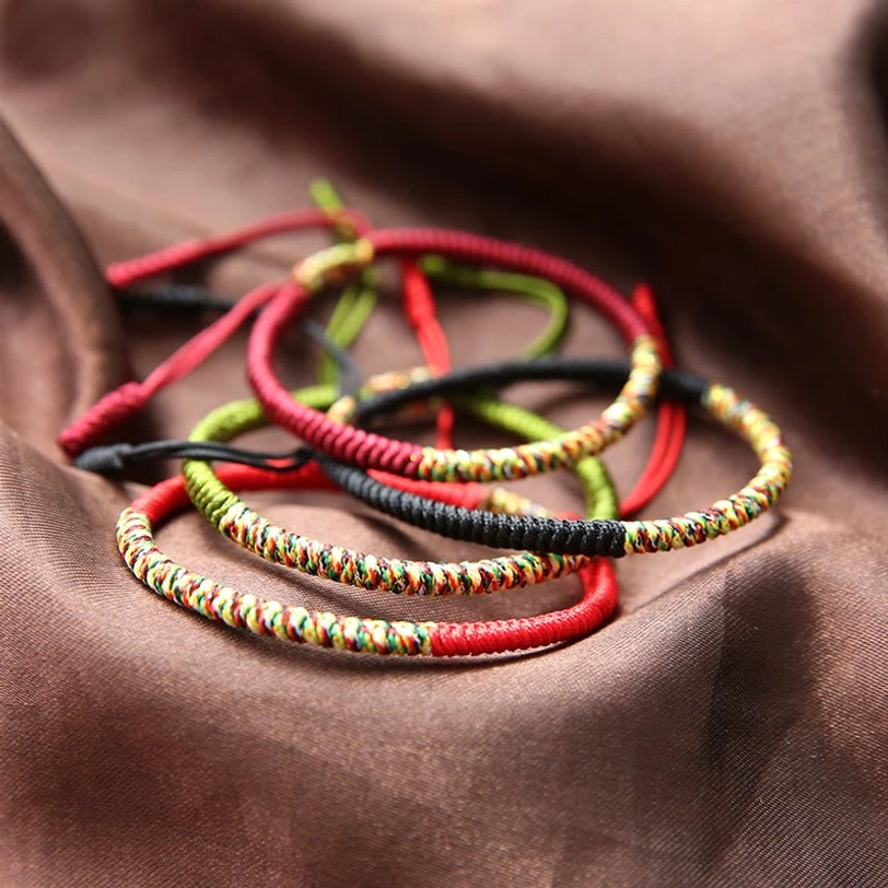 Assorted handmade Tibetan King Kong knot bracelets collection in red, green, black and gold tones, overhead view on brown satin
