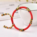 Red adjustable Tibetan King Kong knot protection bracelet with multicolor woven details on white ceramic cup