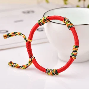 Red adjustable Tibetan King Kong knot protection bracelet with multicolor woven details on white ceramic cup