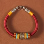 Red handmade Tibetan King Kong Knot protection bracelet with turquoise and yellow beads, silver clasp, flat lay on brown background