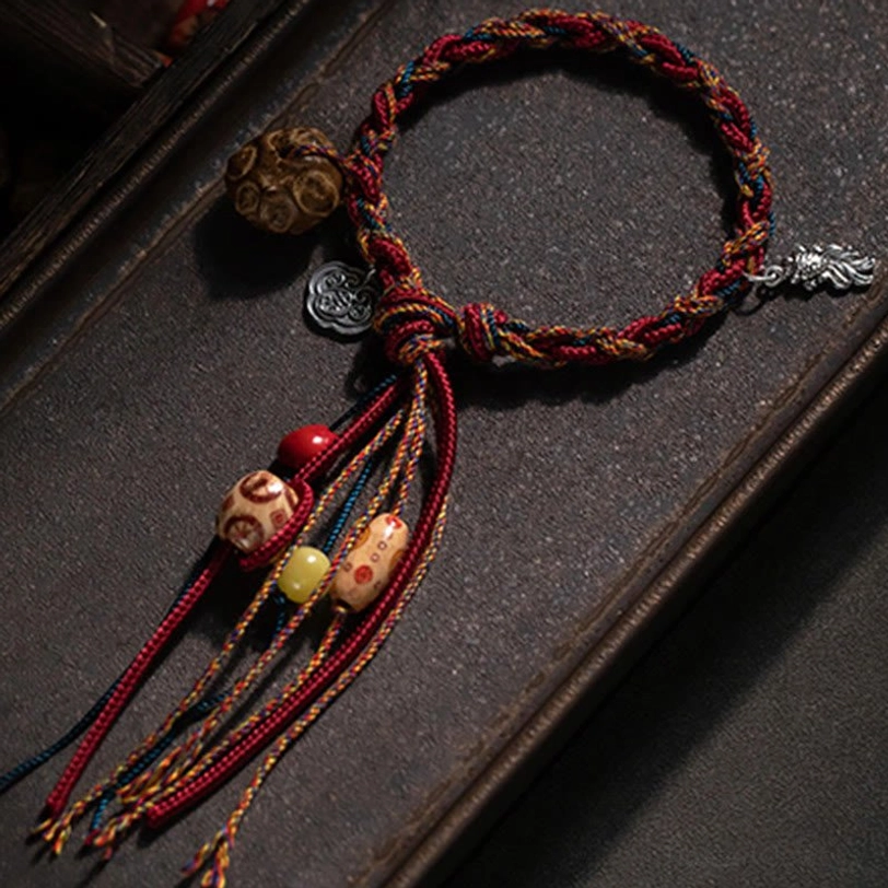 Tibetan koi fish bracelet with silver auspicious cloud charm and dangling tassel accents on dark wooden tray