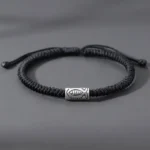 Tibetan koi fish black string bracelet flat lay with silver engraved fish charm on gray background