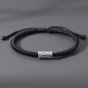 Tibetan koi fish black string bracelet flat lay with silver engraved fish charm on gray background