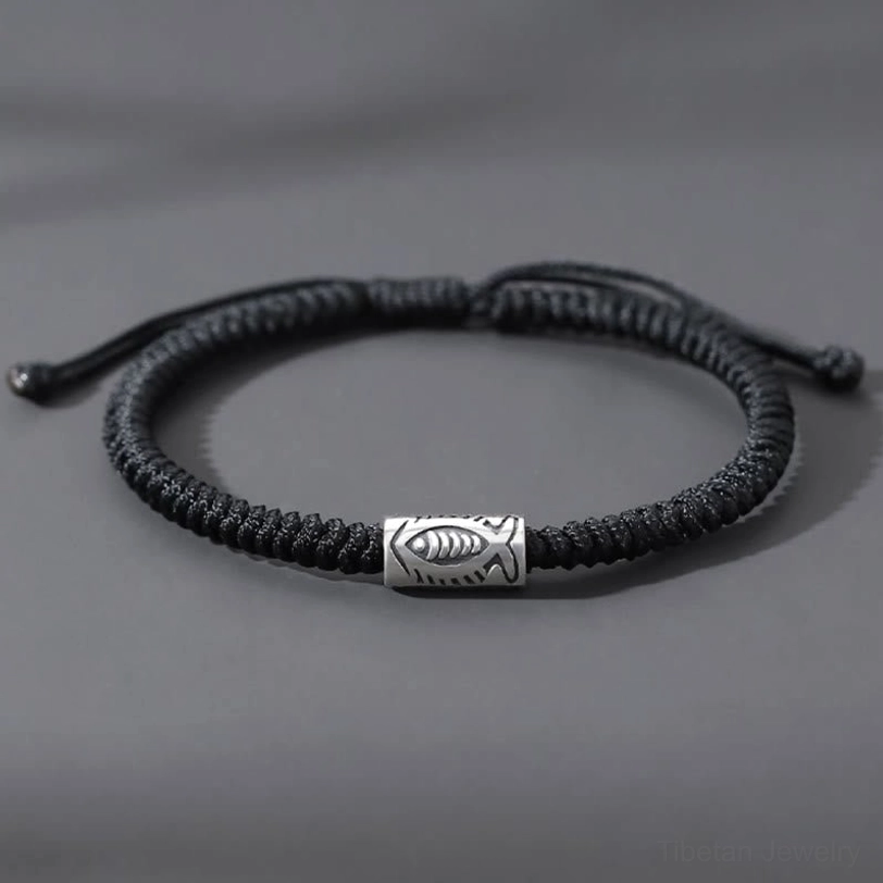 Tibetan koi fish black string bracelet flat lay with silver engraved fish charm on gray background