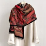 Tibetan landscape painting scarf shawl with hand-knotted black tassels draped over shoulder, featuring traditional red mountain waterfall motif and frayed hem detail