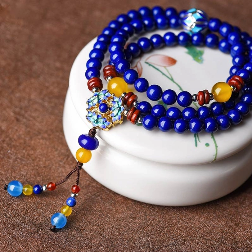 Tibetan Lapis Lazuli beaded bracelet with enamel pendant, wooden spacers, and colored tassel on white ceramic