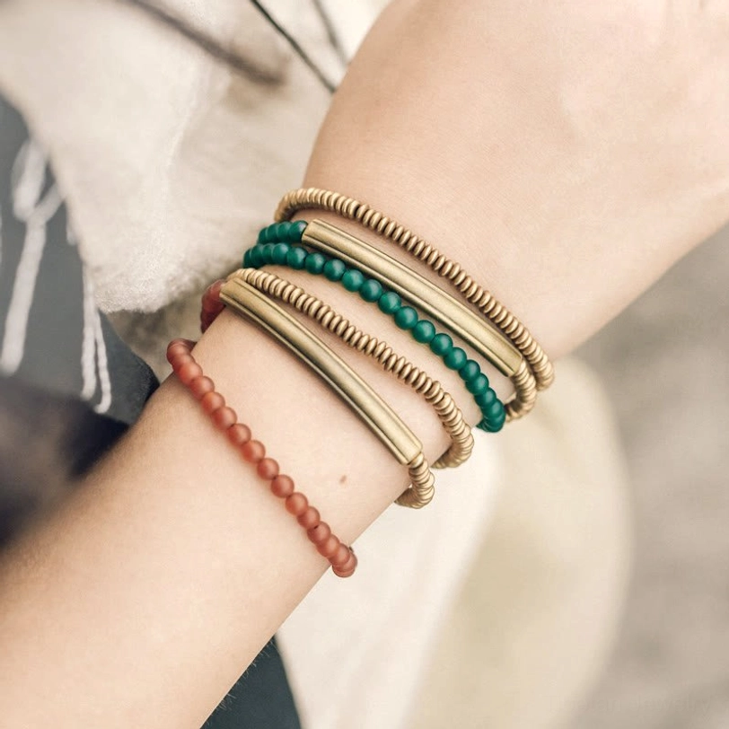 Stacked layered Tibetan bracelets with red agate, brass cuffs, and green beads overhead close-up