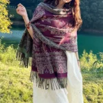 Woman wearing purple Tibetan botanical shawl with leaf paisley patterns at sunny lakeside, front three-quarter view