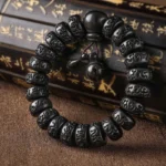 Tibetan lightning strike wood prayer bracelet with carved Om Mani Padme Hum mantra beads and wooden bell charm, overhead view on calligraphy scroll