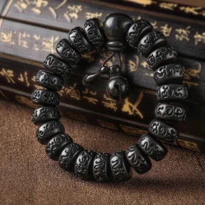 Tibetan lightning strike wood prayer bracelet with carved Om Mani Padme Hum mantra beads and wooden bell charm, overhead view on calligraphy scroll