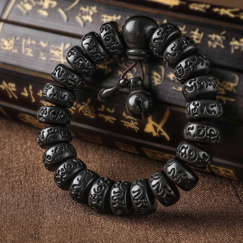 Tibetan lightning strike wood prayer bracelet with carved Om Mani Padme Hum mantra beads and wooden bell charm, overhead view on calligraphy scroll