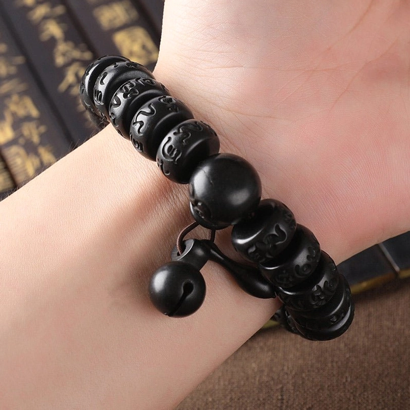 Tibetan lightning strike wood bracelet worn on wrist in close-up, displaying hand-carved mantra beads and bell charms with spiritual calligraphy backdrop