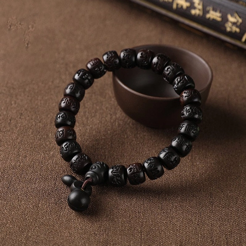 Single Tibetan lightning strike wood bracelet with dangling bell charm on brown fabric background, flat lay side view