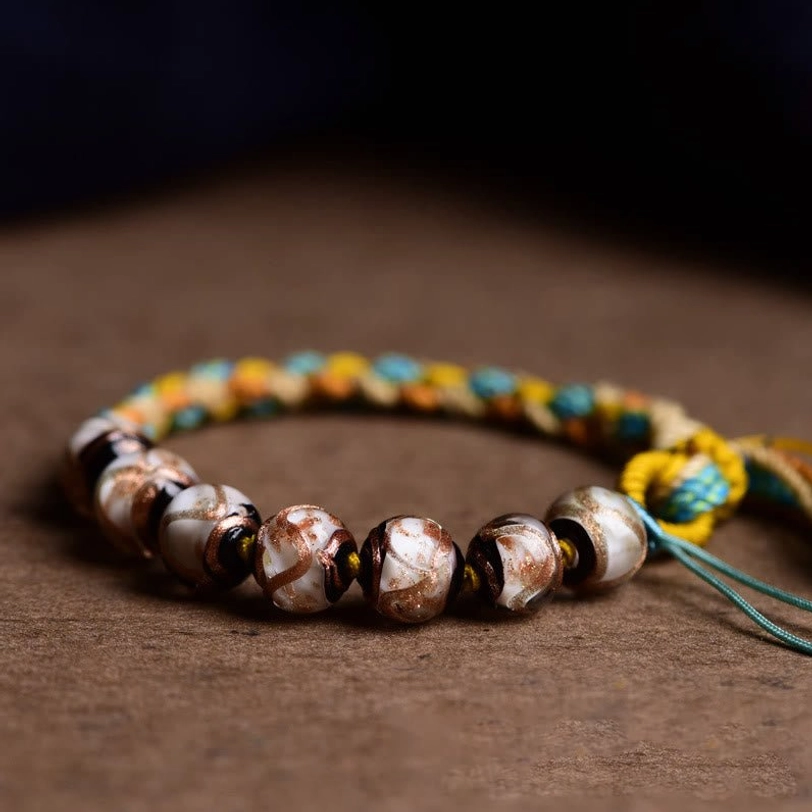 Close-up detail of Tibetan fortune bracelet showing thick ceramic liuli beads with brown and white pattern, vibrant woven rope on wooden table