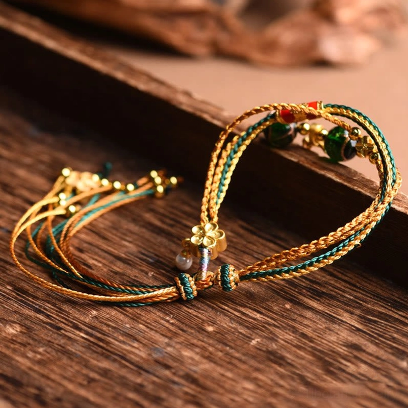 Close-up macro detail of Tibetan liuli glass healing bracelet showing glitter dark green glass beads golden metal hardware and red enamel trim