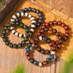 Multicolor Tibetan liuli glass bead bracelets collection with red, blue, green, white and brown glazed beads featuring metallic accents, displayed in flat lay on wooden vintage mat