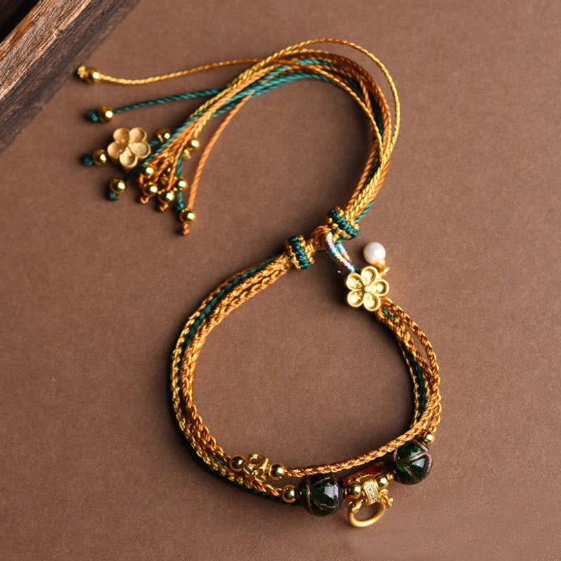 Handmade Tibetan healing bracelet overhead angle on wooden surface displaying braided cords flower charm tassel pendant and pearl accent details