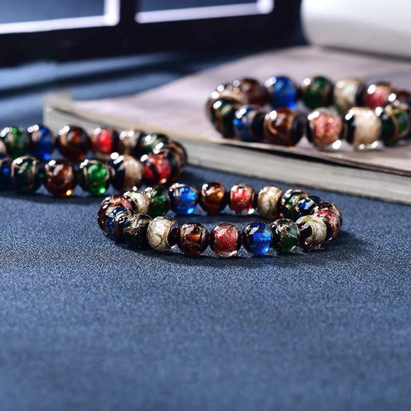 Multiple loose Tibetan colored glaze bracelets with mixed jewel-tone beads scattered on dark blue cloth and vintage book