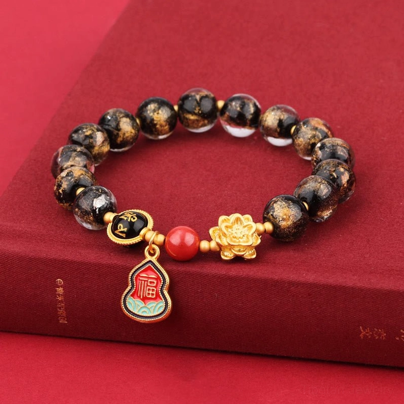 Handcrafted Tibetan Liuli glass beaded bracelet with spotted beads and sacred Sanskrit charm displayed on red book surface