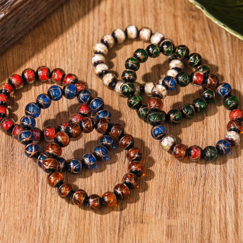 Two Tibetan liuli glass bead bracelets showing color variants with reddish-brown plus blue and white plus dark green plus blue combinations on wooden desktop