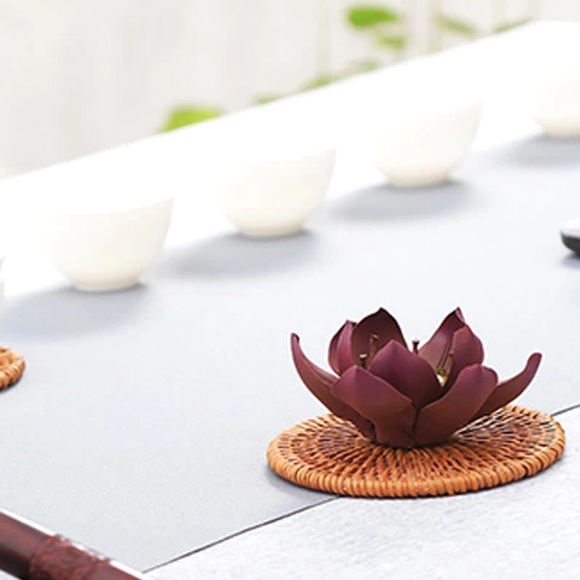 Deep maroon Tibetan lotus burner placed on woven rattan coaster, three-quarter side angle showcasing petal detail