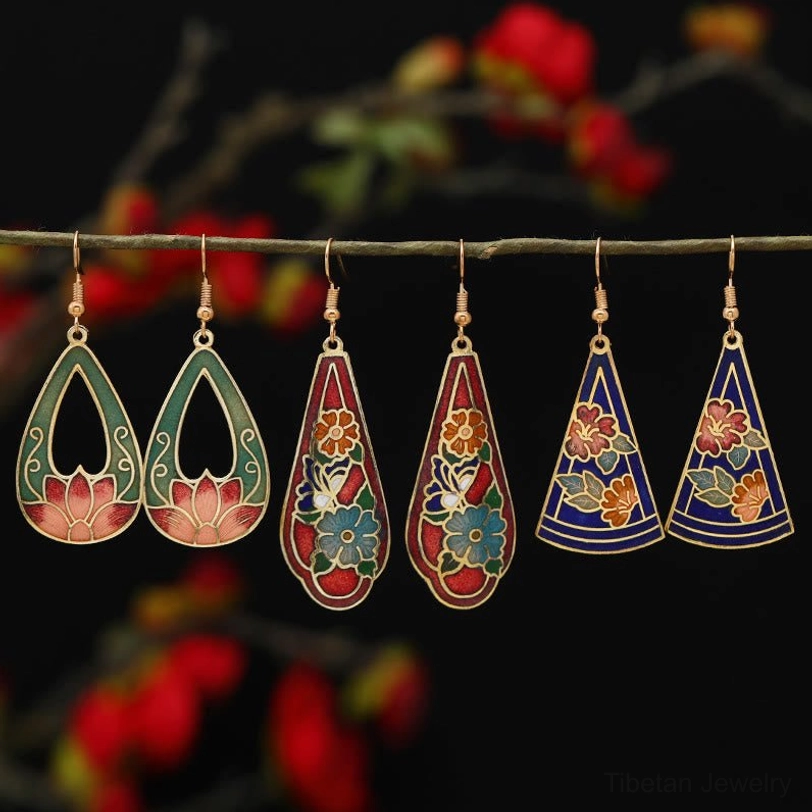 Six pairs of assorted Tibetan lotus and butterfly enamel drop earrings in multiple colors displayed on twig, feng shui symbol jewelry collection
