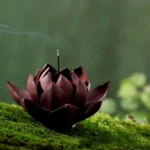 Handcrafted Tibetan lotus purple clay incense burner with deep maroon layered petals, side high-angle view on natural moss ground