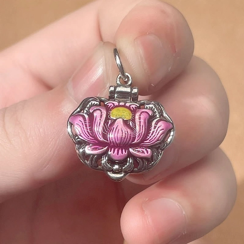 Pink enamel lotus locket pendant held in hand showing hinged design and vintage copper finish