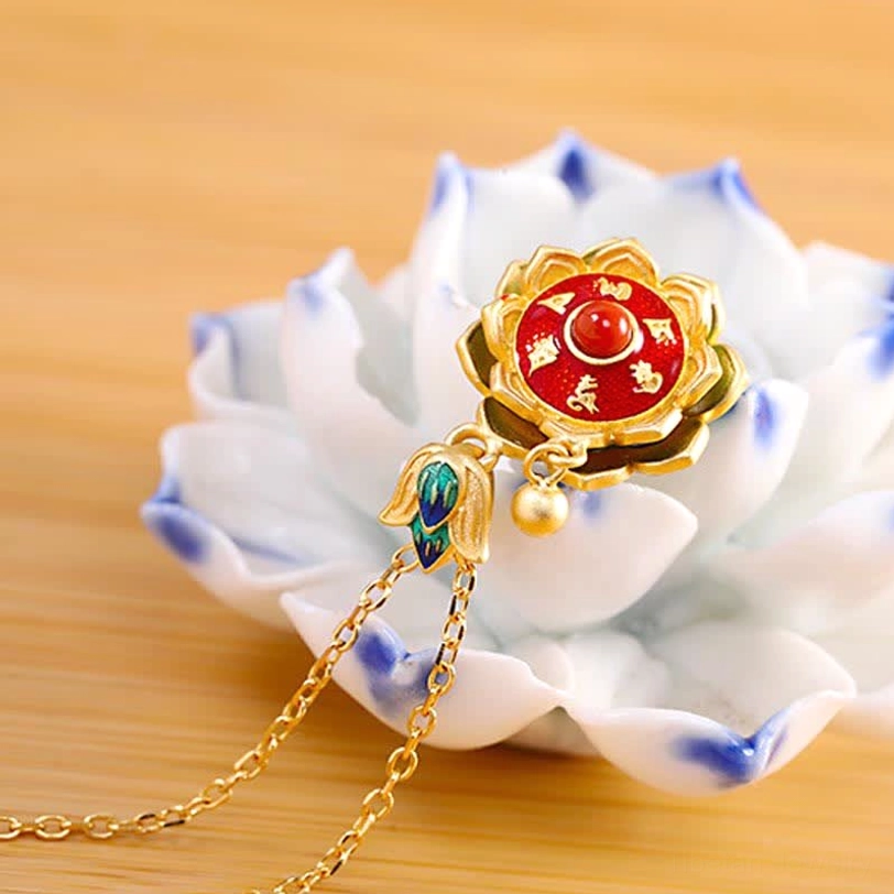 Tibetan prayer wheel necklace with gold chain and red agate lotus pendant, displayed alongside blue-and-white porcelain lotus ornament on wooden surface