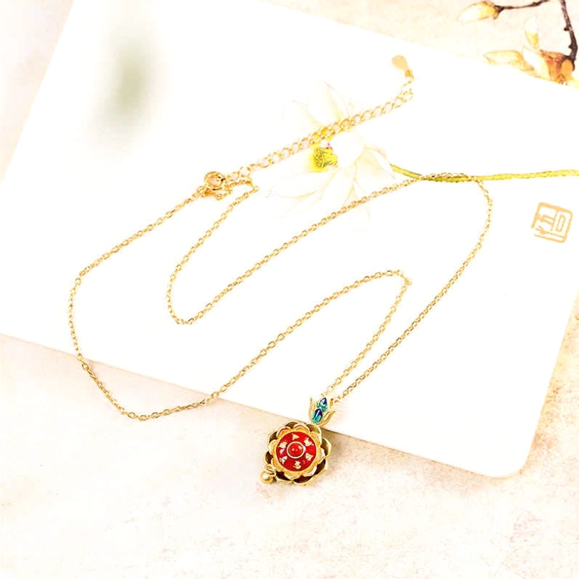 Single Tibetan lotus prayer wheel pendant necklace with delicate gold chain and red agate center stone, top-down flat lay photography on wooden desktop