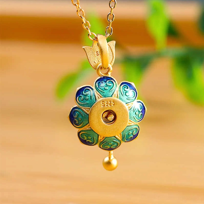 Back view of sterling silver lotus prayer wheel pendant with intricate cloisonné petals, 925 hallmark, and decorative gold bead, displayed on wooden desktop