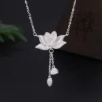 999 sterling silver lotus flower pod pendant with carved details and tassel charm, top-down studio view on dark background